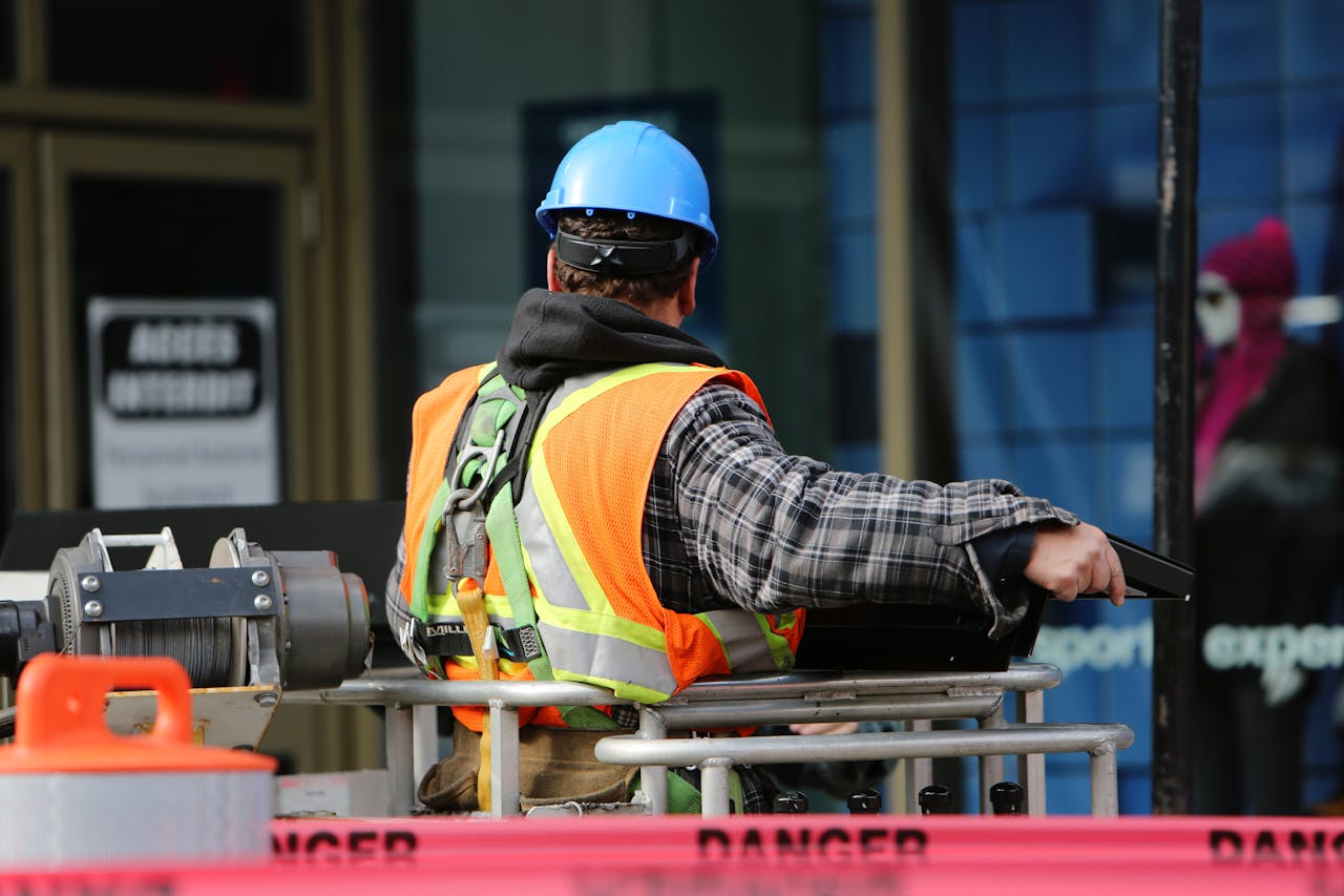 our-services-3 A construction worker wearing a blue helmet and safety vest operates equipment at an urban construction site.